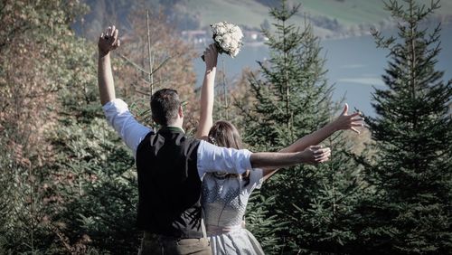 Rear view of couple with arms raised standing against trees