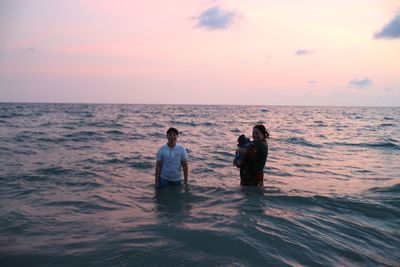 Women with friend holding pug in sea during sunset