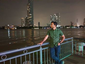 Full length of man standing by railing in city at night