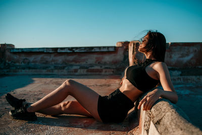 Side view of woman sitting on sofa against sky