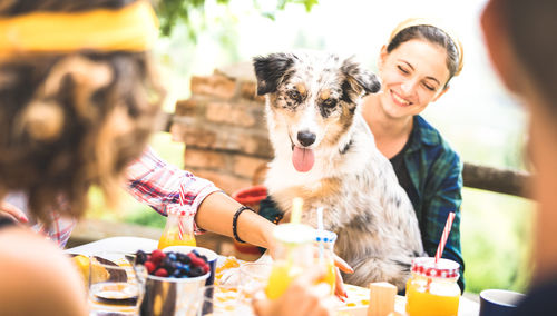 Cheerful woman sitting with dog while having food and drinks at outdoor restaurant