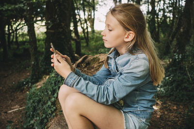 Side view of blond girl using smart phone in forest