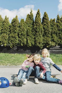 Portrait of happy boys and girl enjoying on skateboard against trees
