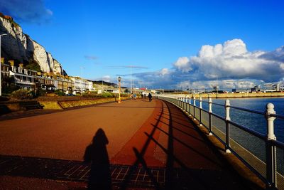 Shadow of people on footpath by railing against blue sky