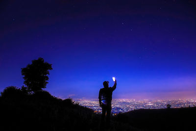 Rear view of silhouette man taking selfie on mountain against blue sky at night