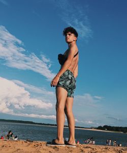 Low angle view of young man standing on beach against blue sky