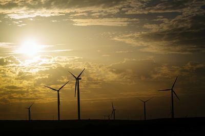 Silhouette windmills on landscape against sky during sunset