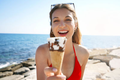 Close-up of brazilian woman smiling at camera showing ice cream cone on the beach on summertime