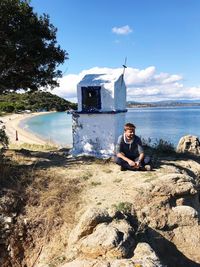 Man sitting on rocks by sea against sky