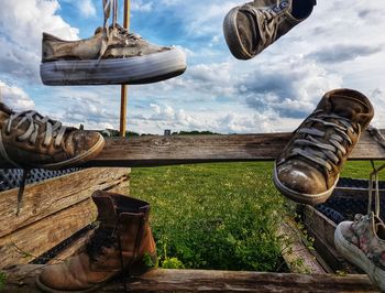 Low section of old shoes on field against sky