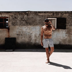 Full length of shirtless man standing against wall