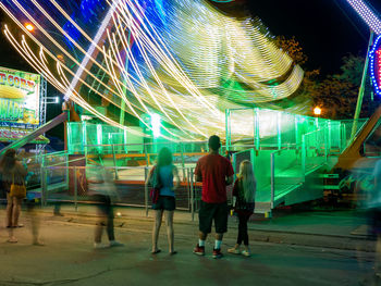 Rear view of people walking in amusement park at night