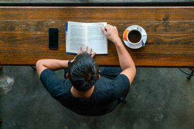 High angle view of woman holding coffee while sitting on table