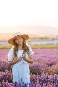 Cute child girl 8-9 year old with long blonde hair wear straw hat in bloom lavender field outdoor