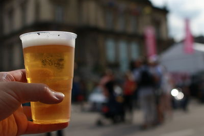 Close-up of human hand holding beer in city
