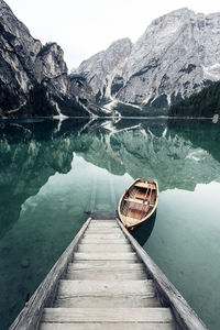 Boat moored by jetty on lake against mountain