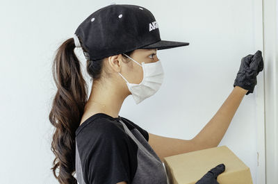 Side view of young woman holding hat against wall