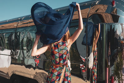 Woman holding blue scarf standing against bus