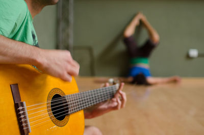 Midsection of man playing guitar against woman dancing at home