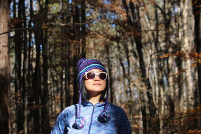 Woman wearing sunglasses standing against trees in forest