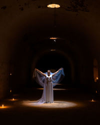 Lady in white bride dress like an angel at a religious mass with burning torches in the dungeon