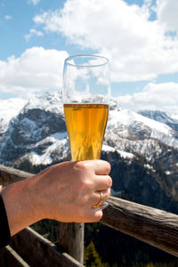 Close-up of hand holding beer glass against mountains