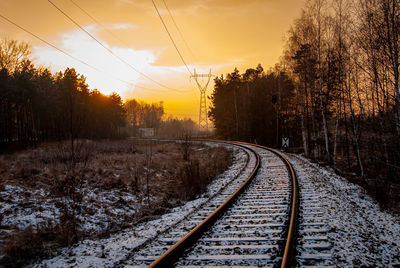 Railroad tracks in snow covered landscape during sunset