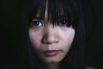 Close-up portrait of serious young woman against black background