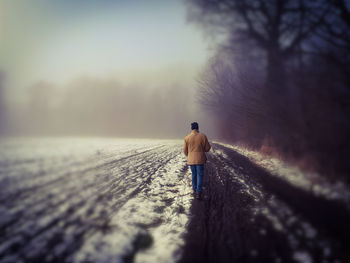 Rear view of man standing on snow covered tree