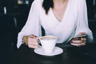 Midsection of woman holding coffee cup on table