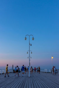 People walking on street against clear blue sky