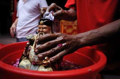 Midsection of man cleaning figurine in bucket