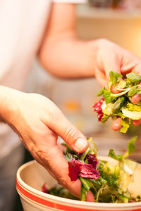 Cropped hand of woman making salad in bowl on table