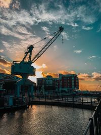 Cranes at commercial dock against sky during sunset