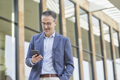 Smiling businessman using mobile phone outside building