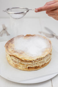 Cropped hand sprinkling powdered sugar on dessert