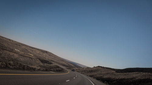 Road leading towards mountains against clear blue sky