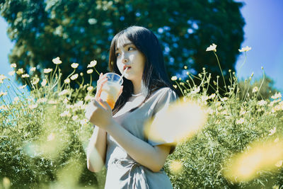 Young woman in drinking glass while standing by plants