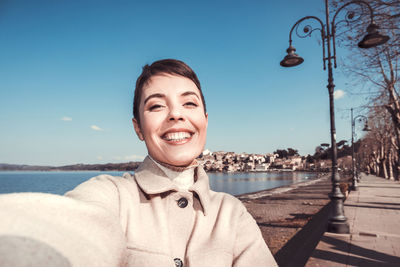 Beautiful young woman with short hair is taking a selfie in front of the lake.