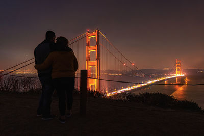 People at illuminated bridge against sky during sunset