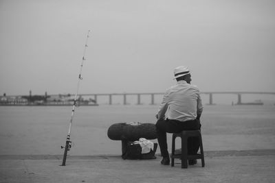 Rear view of man fishing in sea against clear sky