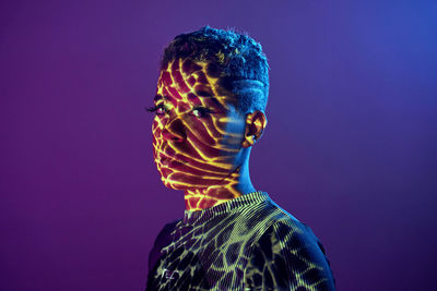 Charming african american female with short hair and in shadow projector light on face looking at camera on purple background in studio