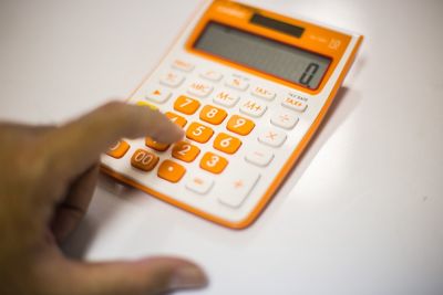 Cropped hand of person using calculator on white table