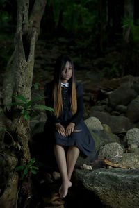 Full length of woman sitting on rock in forest