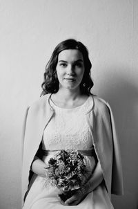 Portrait of bride holding bouquet against wall