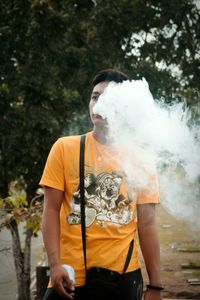 Midsection of man holding cigarette against tree