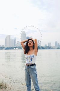 Portrait of beautiful young woman standing against sea in city