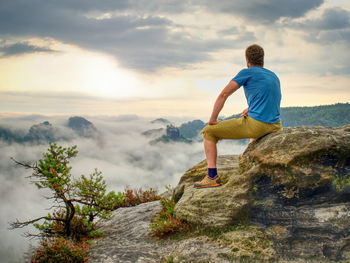 Hiker in middle of nowhere and thinking alone. man sit on top of a sharp peak enjoying sunrise.