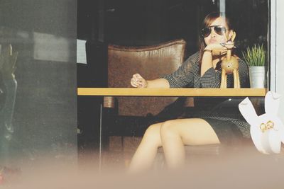 Reflection of woman in sunglasses sitting on chair at home