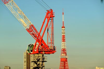 Low angle view of tokyo tower and crane against clear sky in city